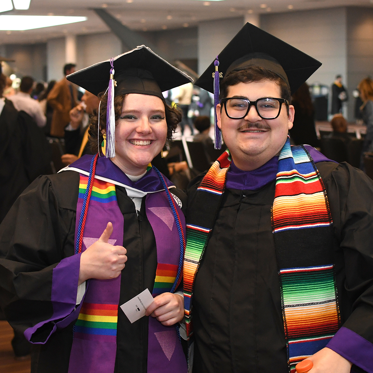 Two graduating students in caps and gowns pose for a photo, smiling