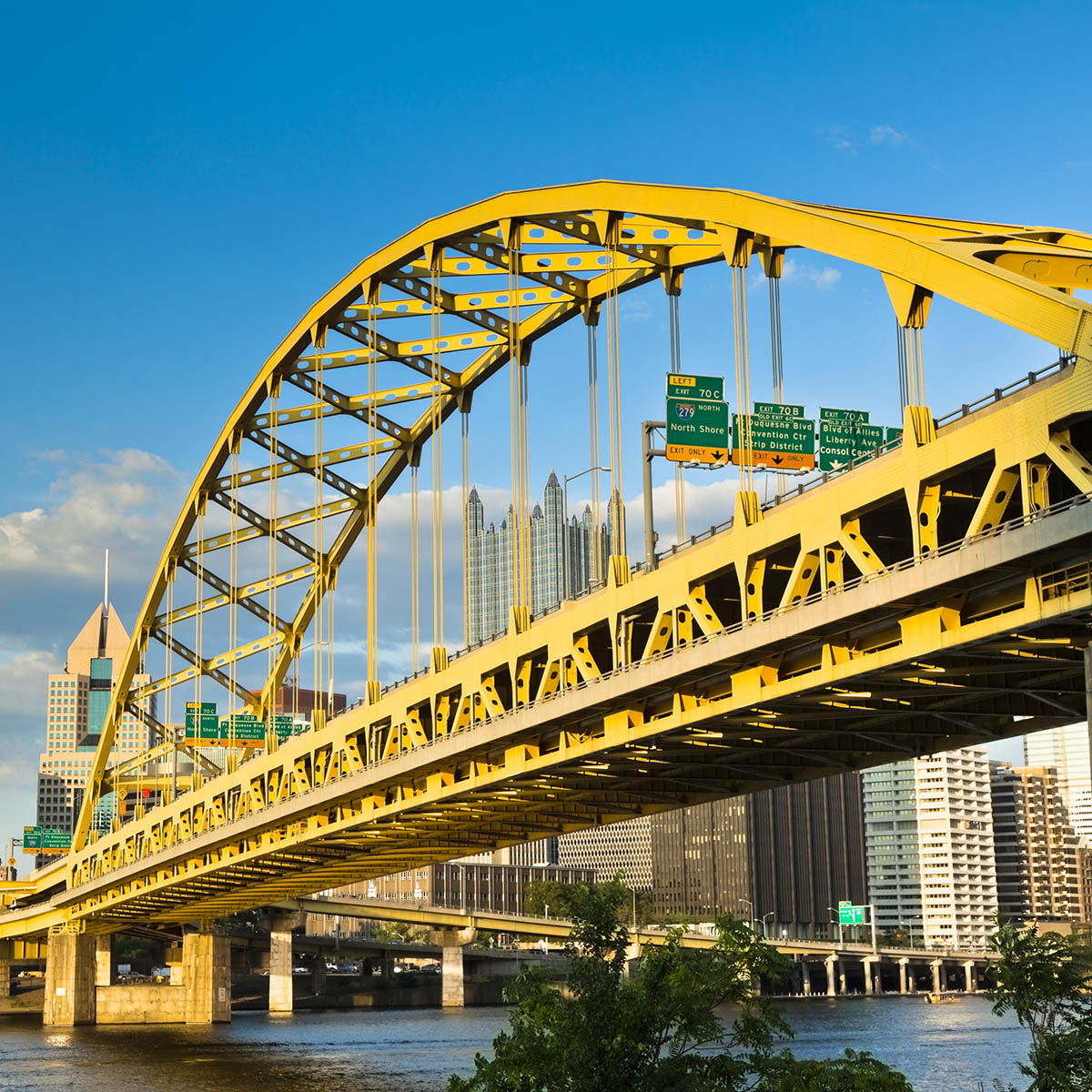 Bright photo of a yellow bridge in Pittsburgh on a sunny day against blue sky