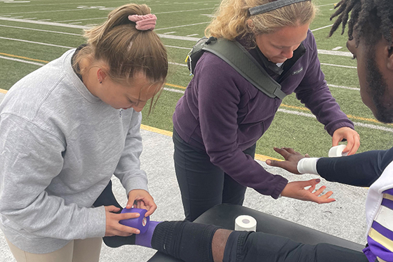 Two MSAT students wrap injuries on an athlete