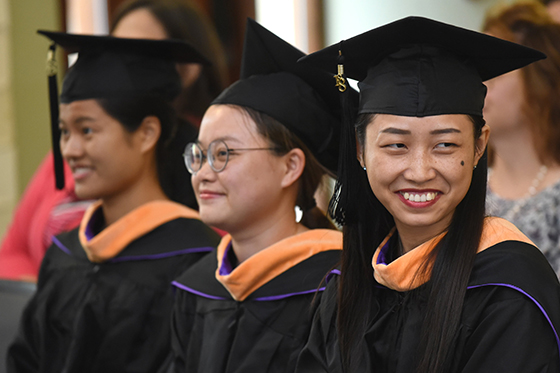 Photo of three Chatham University international students at graduation in caps and gowns