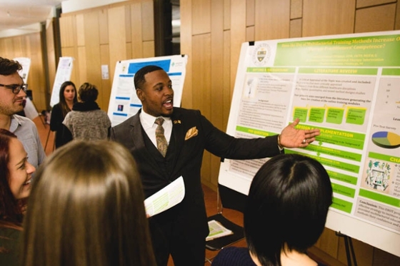 Photo of a man in a suit presenting a poster to a group of people. 