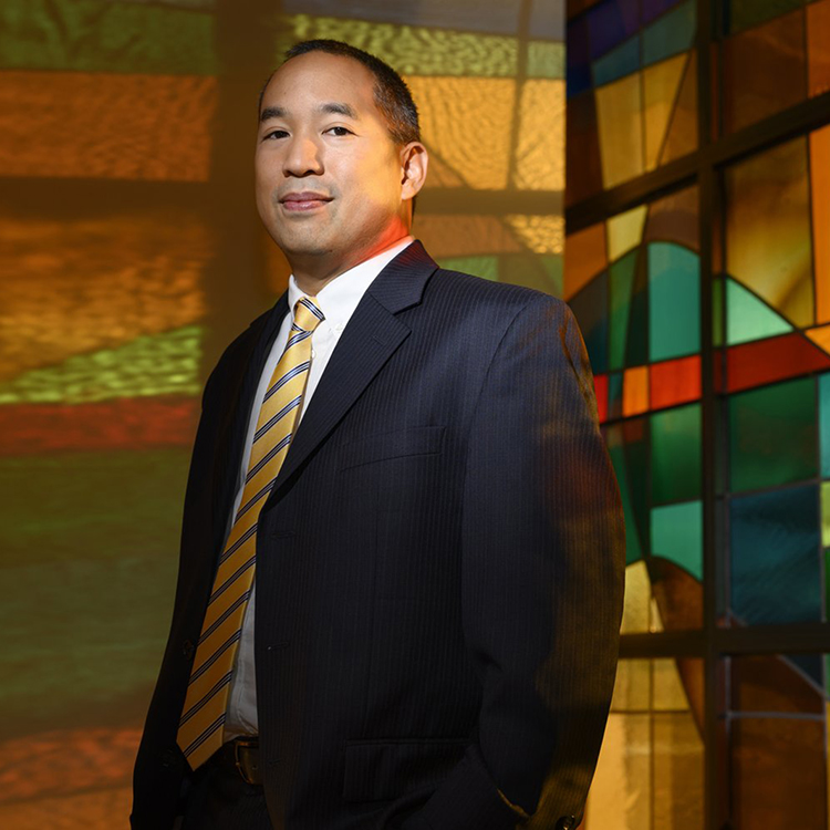 Portrait of a man in a suit standing in front of a a colorful, abstract background