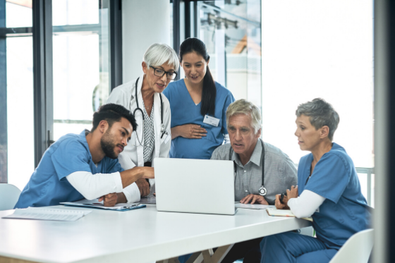 Photo of a group of doctors and nurses standing around a laptop and having a conversation.