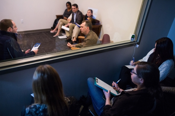 Photo of Chatham University psychology students sitting behind a mirrored window observing a therapy session. 