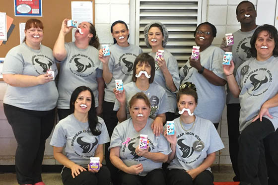 Photo of a group of volunteers wearing the same grey shirt, with fake milk mustaches, each holding a small carton of milk