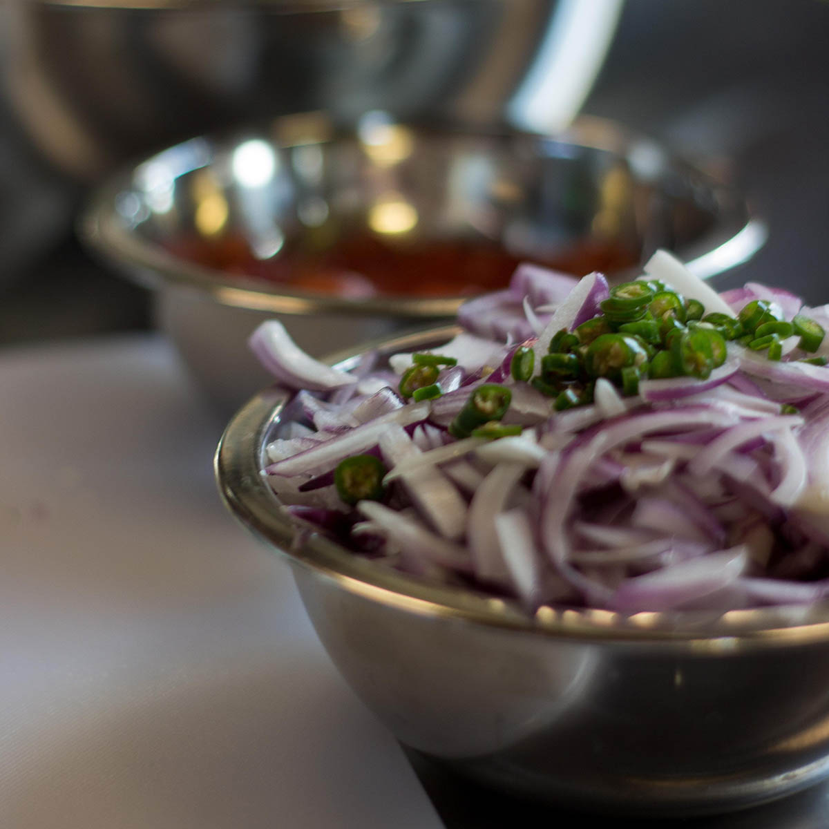 Close-up photo of chopped red onion topped with a green pepper in a silver mixing bowl