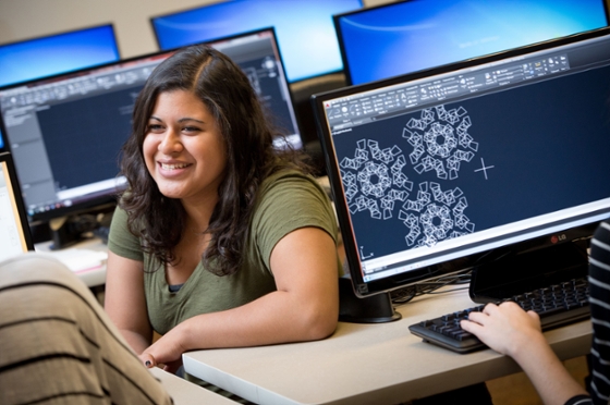 Photo of a Chatham University student sitting between computers in lab smiling. 