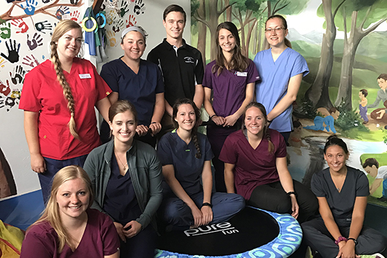 Photo of ten physical therapy students posing together in front of a painted mural in an Ecuadorian childcare facility. 
