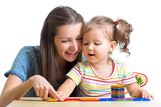 Photo of a woman and toddler leaning together, smiling and working on a puzzle in front of them.