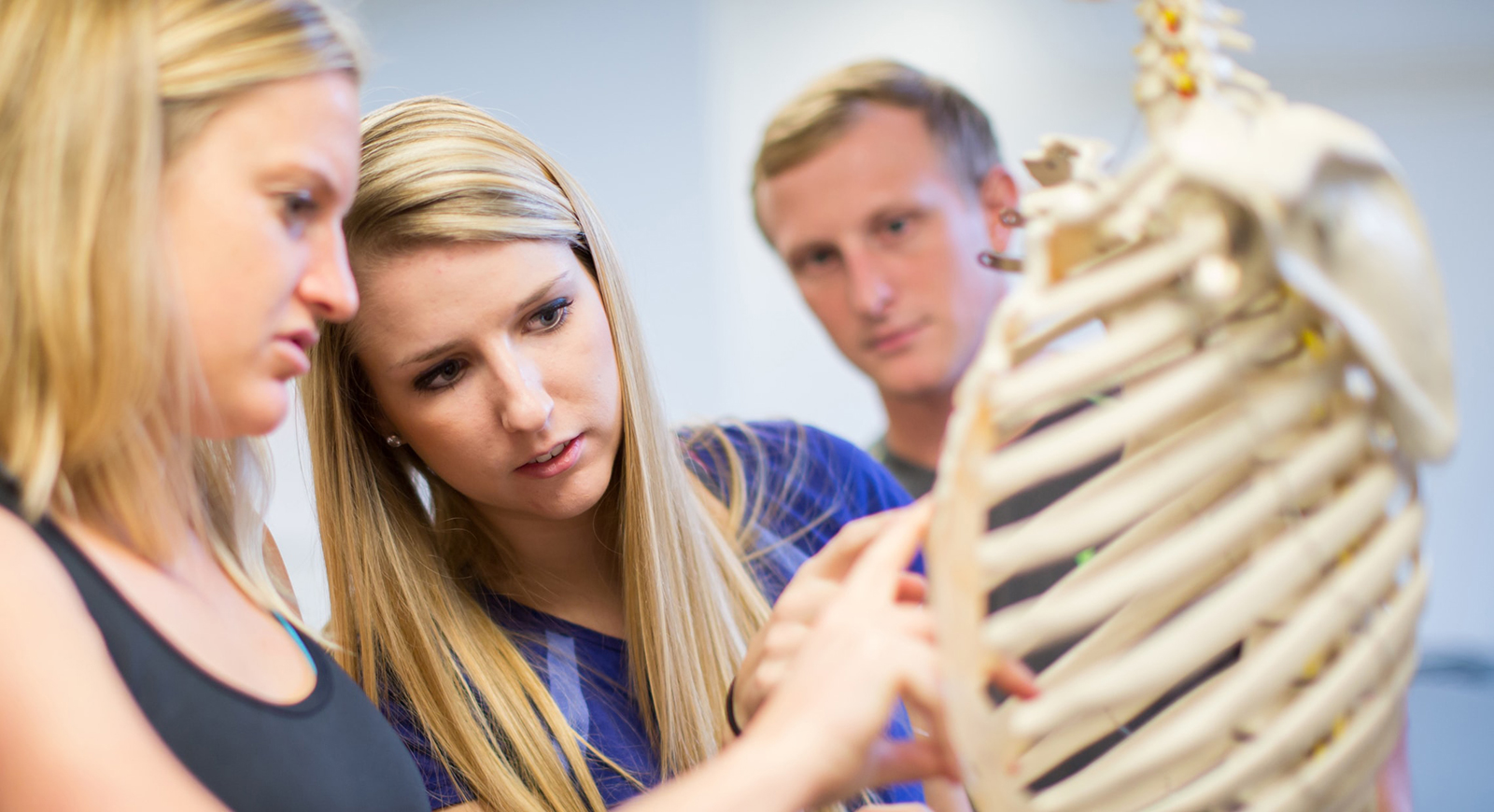 Photo of three Chatham University students examining a classroom skeleton's chest. 