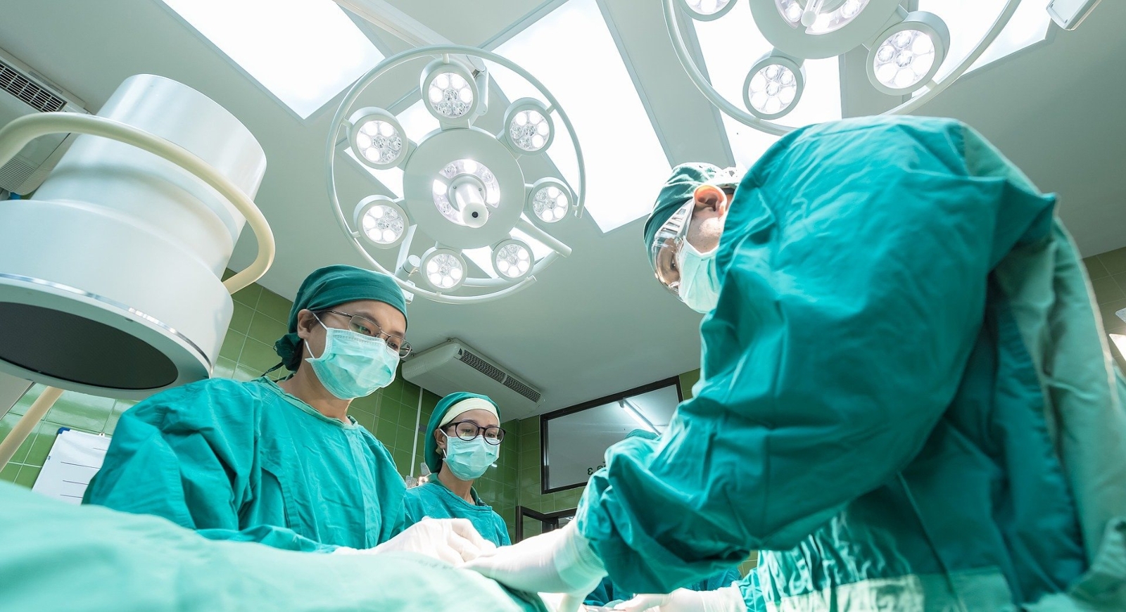Photo angling above, showing surgeons leaning over an operating table and conducting a procedure