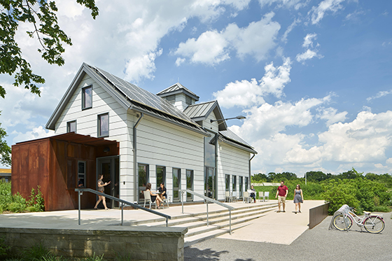 Photo of Chatham University students gathering near the white dairy barn with solar paneled roof at Eden Hall Farm. 