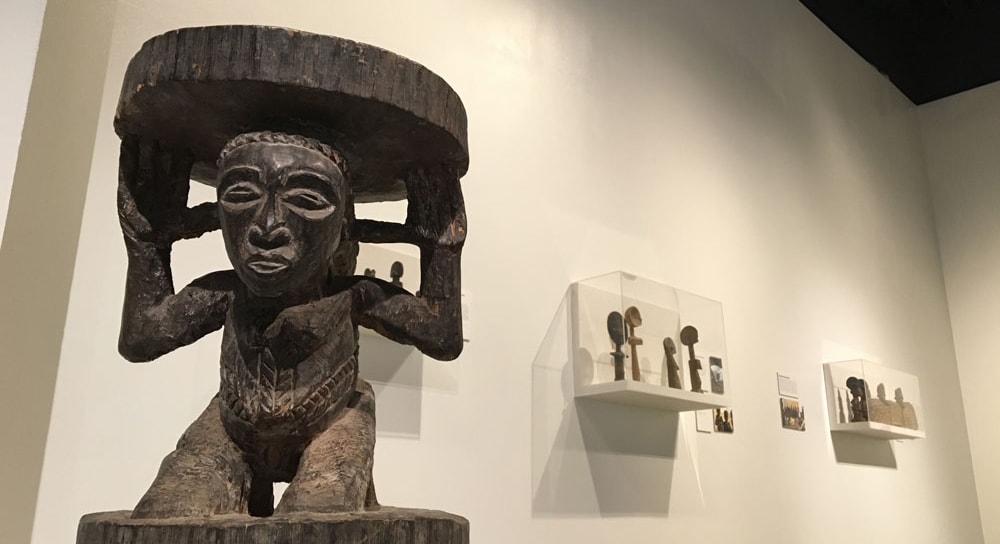 Photo of an African sculpture of a person carrying a plate on their head, in a gallery