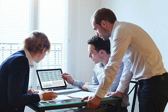 Photo of a group of three business professionals surrounding a computer, working together on a project.