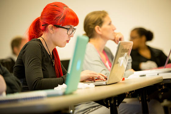 Photo of a student in glasses with bright red hair, working on her laptop in a Chatham University lecture hall