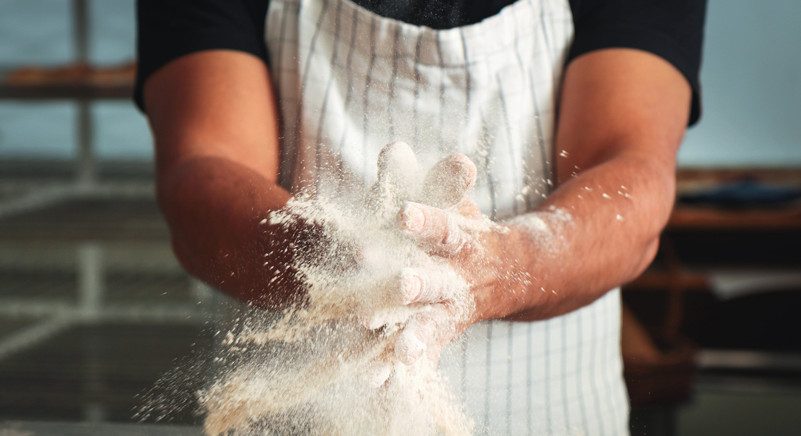 Close-up photo of a man wearing an apron, bringing floured hands together. 