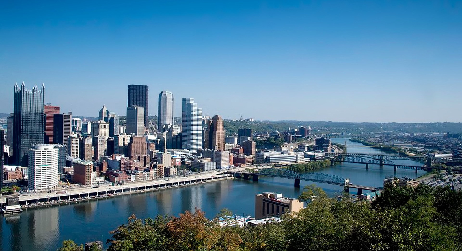 Aerial view of Pittsburgh's city and rivers, with a bright blue sky