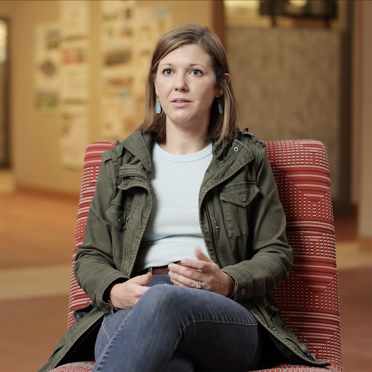 Photo of an alumna seated in a red chair, speaking to a video interviewer