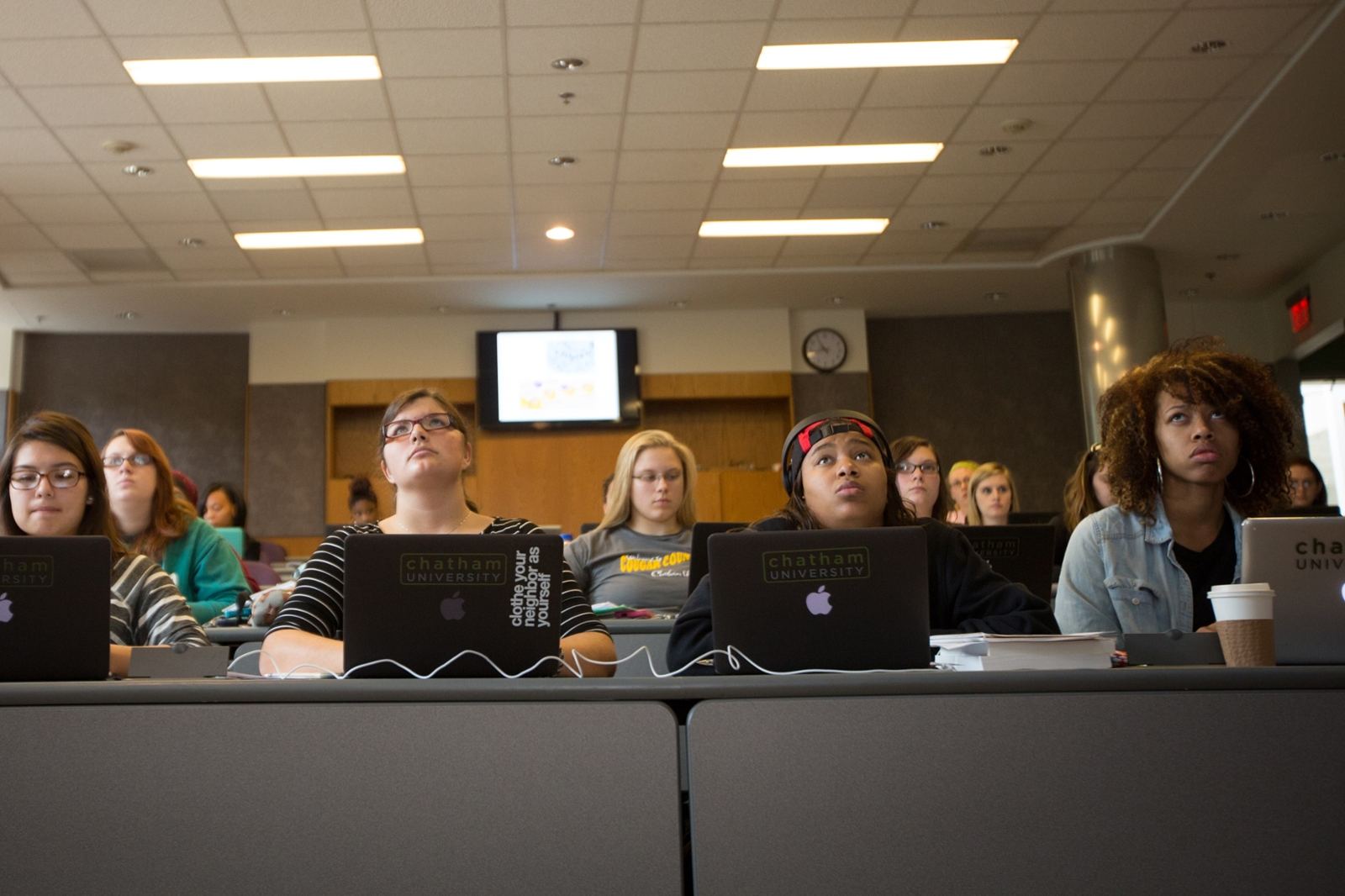 Photo of Chatham University students seated in a tiered lecture hall, with laptops and notebooks open