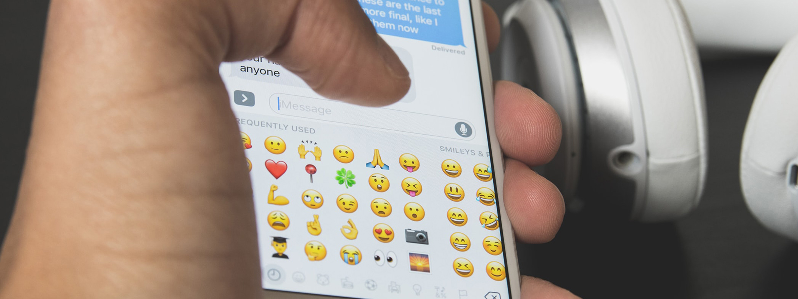 Close-up photo of a hand holding an iPhone while typing on an emoji keyboard.