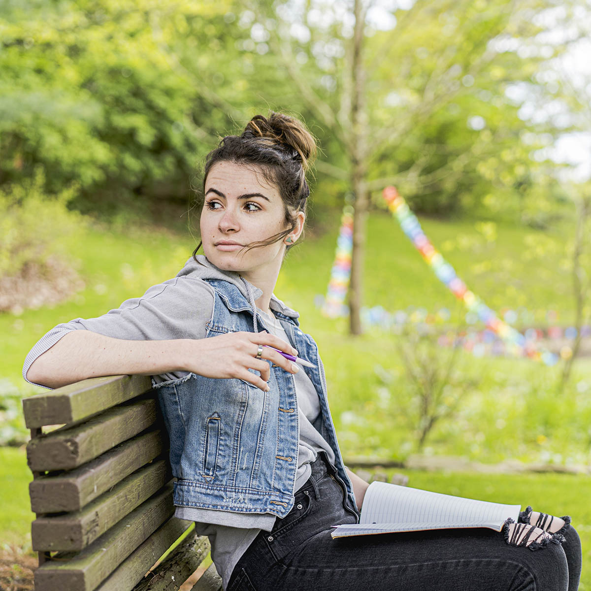 Photo of a female Chatham student with a pencil in hand, seated on a bench outside on Shadyside Campus with an open notebook in her lap