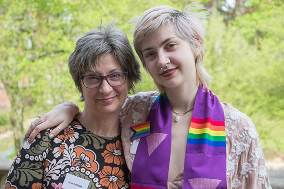 Photo of a graduating Chatham University student wearing a rainbow stole, with an arm over the shoulder of a parent or guardian