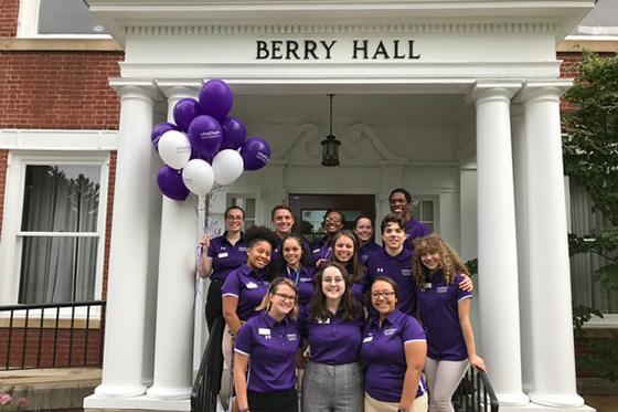 Photo of a group of Chatham University staff standing in front of Berry Hall wearing purple shirts and holding purple balloons. 
