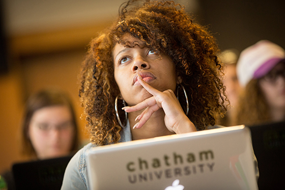 Photo of a female Chatham University student paying attention to a lecture, with a computer in front of her