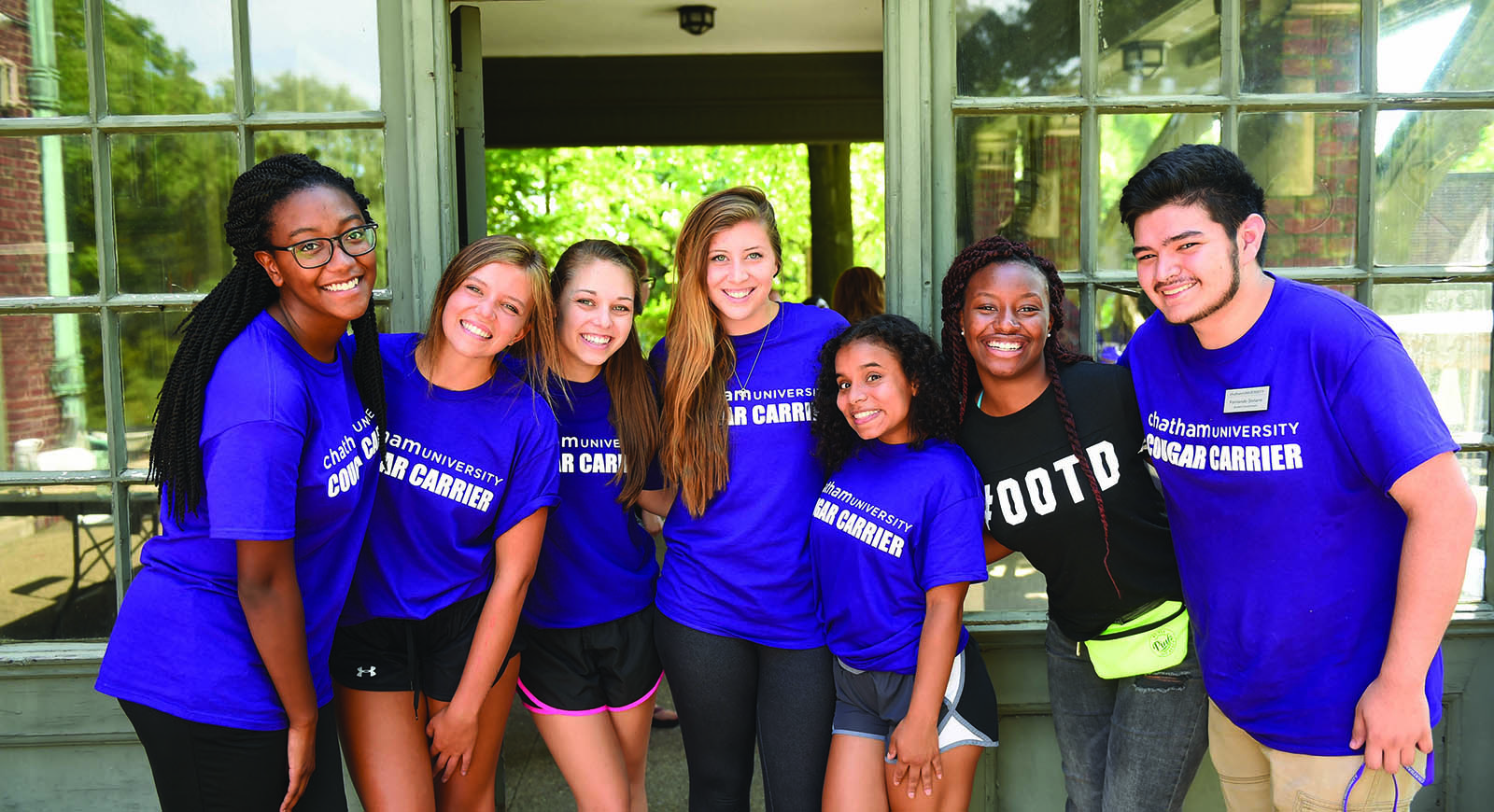 Photo of a group of Chatham University student volunteers, helping a new freshman move into a dorm. They are wearing matching Cougar Carriers shirts.