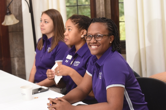 Photo of three Chatham University female students wearing matching purple shirts, preparing to check in people to an event