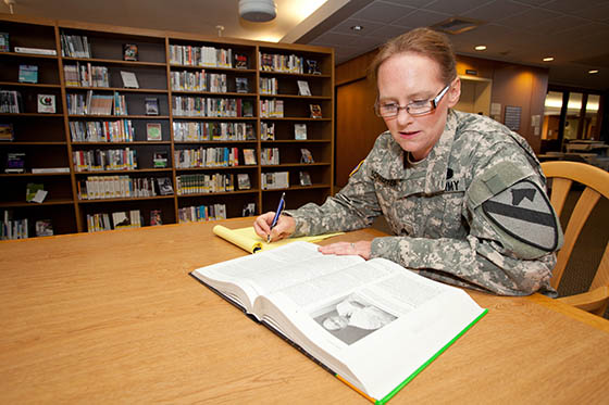 Photo of a female military student in uniform working at a library table