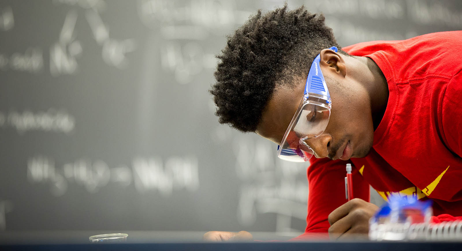 Photo of a student wearing protective goggles, working in a lab