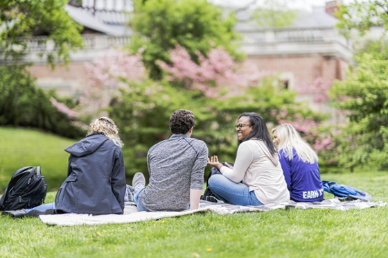 Photo of four Chatham University students sitting outside on a blanket, on Shadyside Campus
