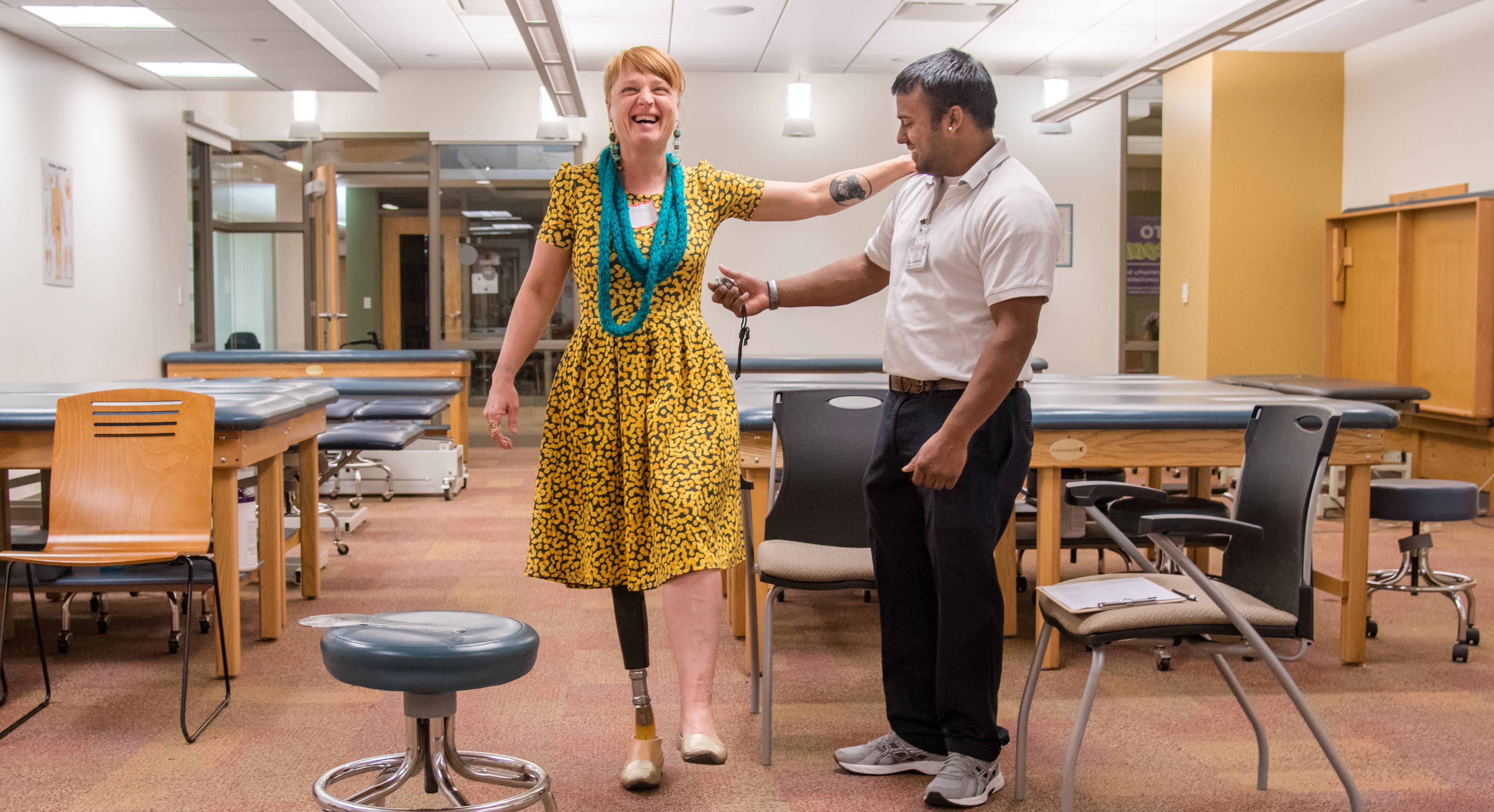 Photo of a Chatham University physical therapy student assisting a woman with a prosthetic leg walk across a physical therapy exercise room.