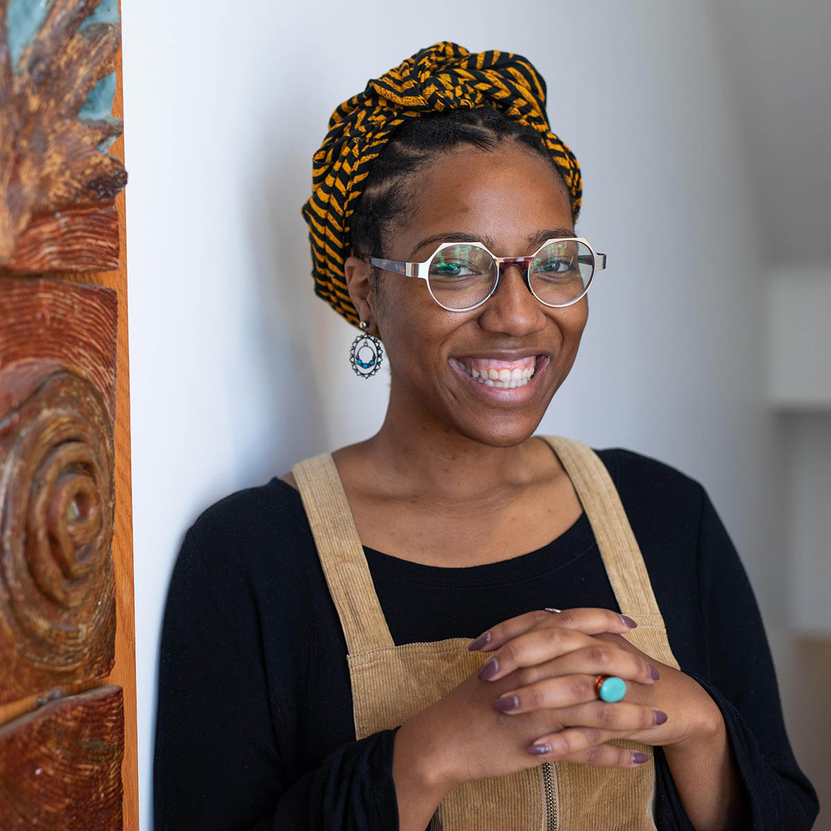 Photo of Ciera Marie Young, a Black woman with hexagonal glasses, smiling in front of a colorful painting