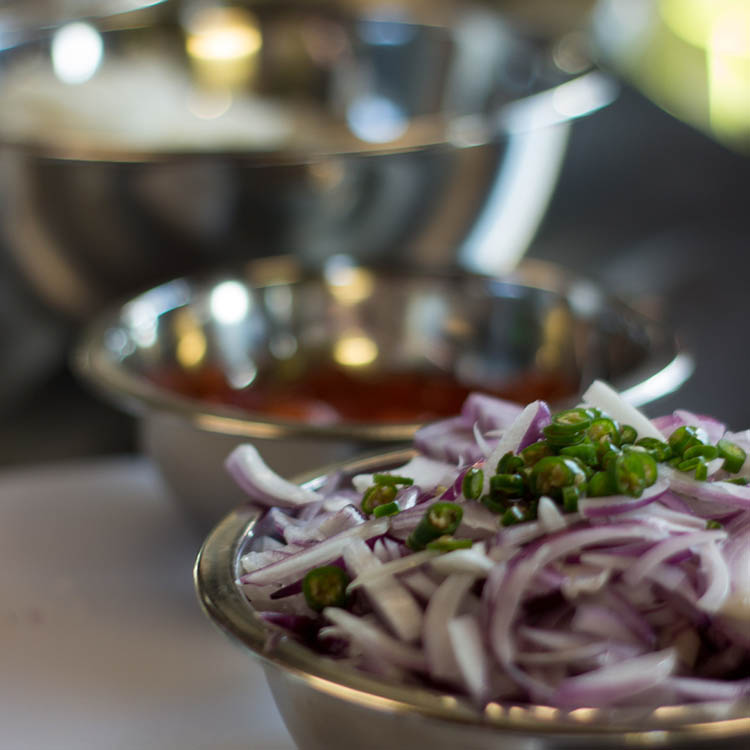 Photo of a few silver food preparation bowls with sauce and sliced red onions