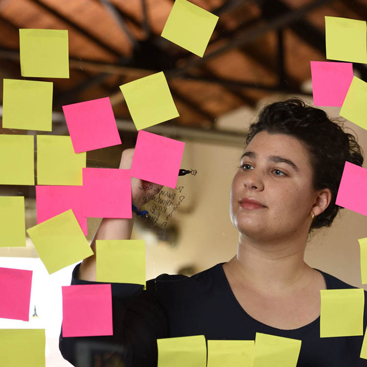 Photo of MBA student Sophie Slesinger writing on a clear plastic wall covered in post-it notes