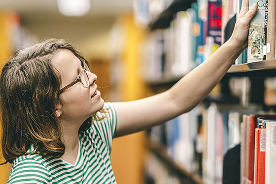 Photo of a female Chatham University student taking a book off of a library shelf