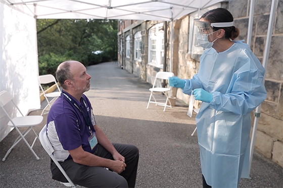 Photo of a medical professional in protective attire explaining a COVID-19 test to Dr. Finegold outside of Health Services