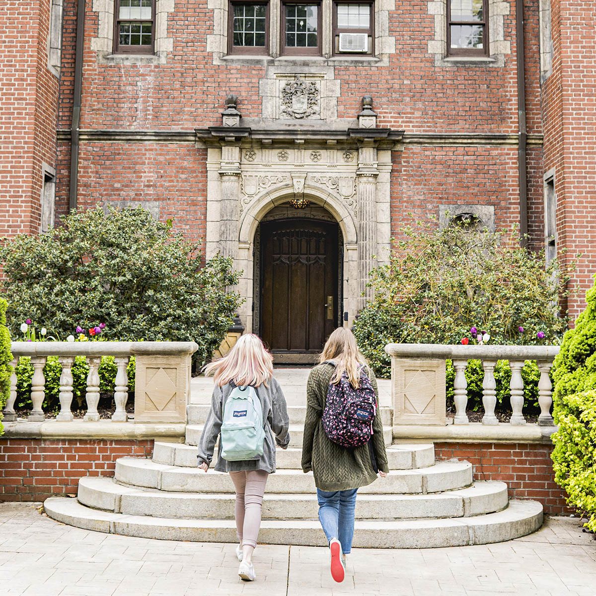 Photo of two young women with backpacks walking into a residence hall